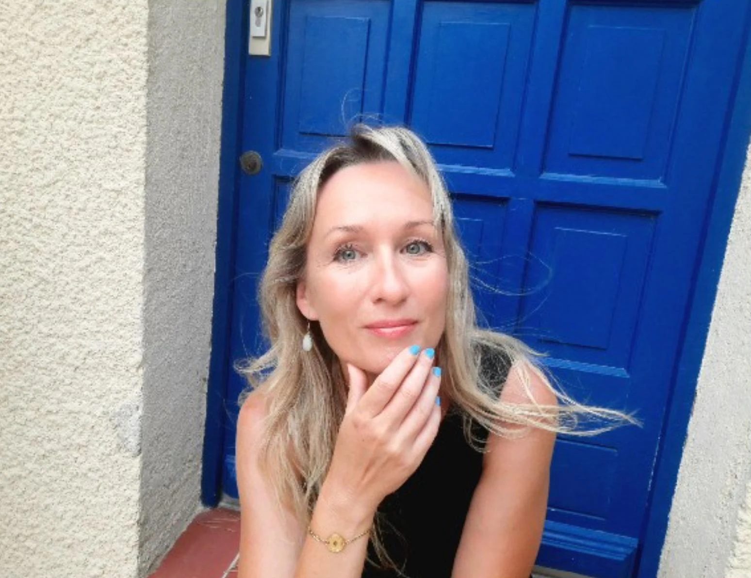 Heike Hähnlein vor einer blau gestrichenen Holztür, die Hand nachdenklich am Kinn